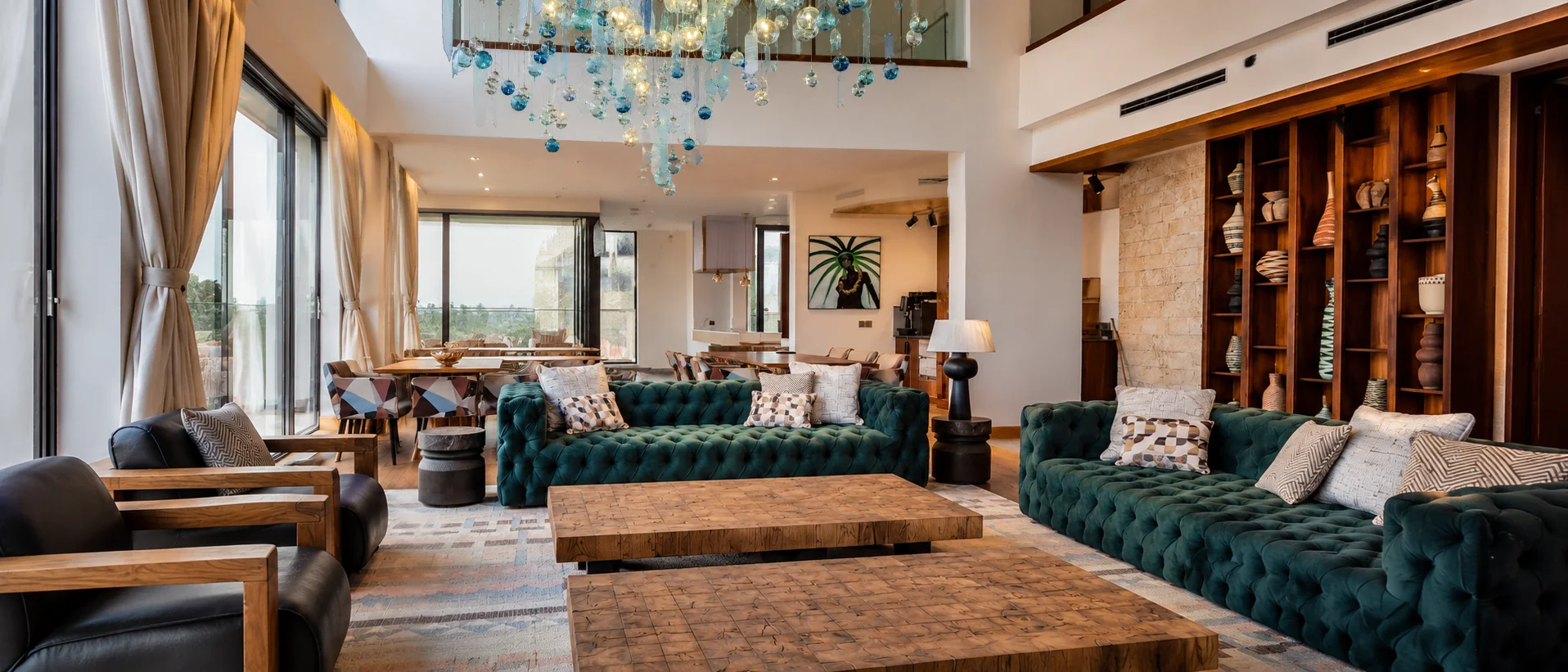 Open-plan interior with teal sofas, carved timber tables and a suspended glass chandelier