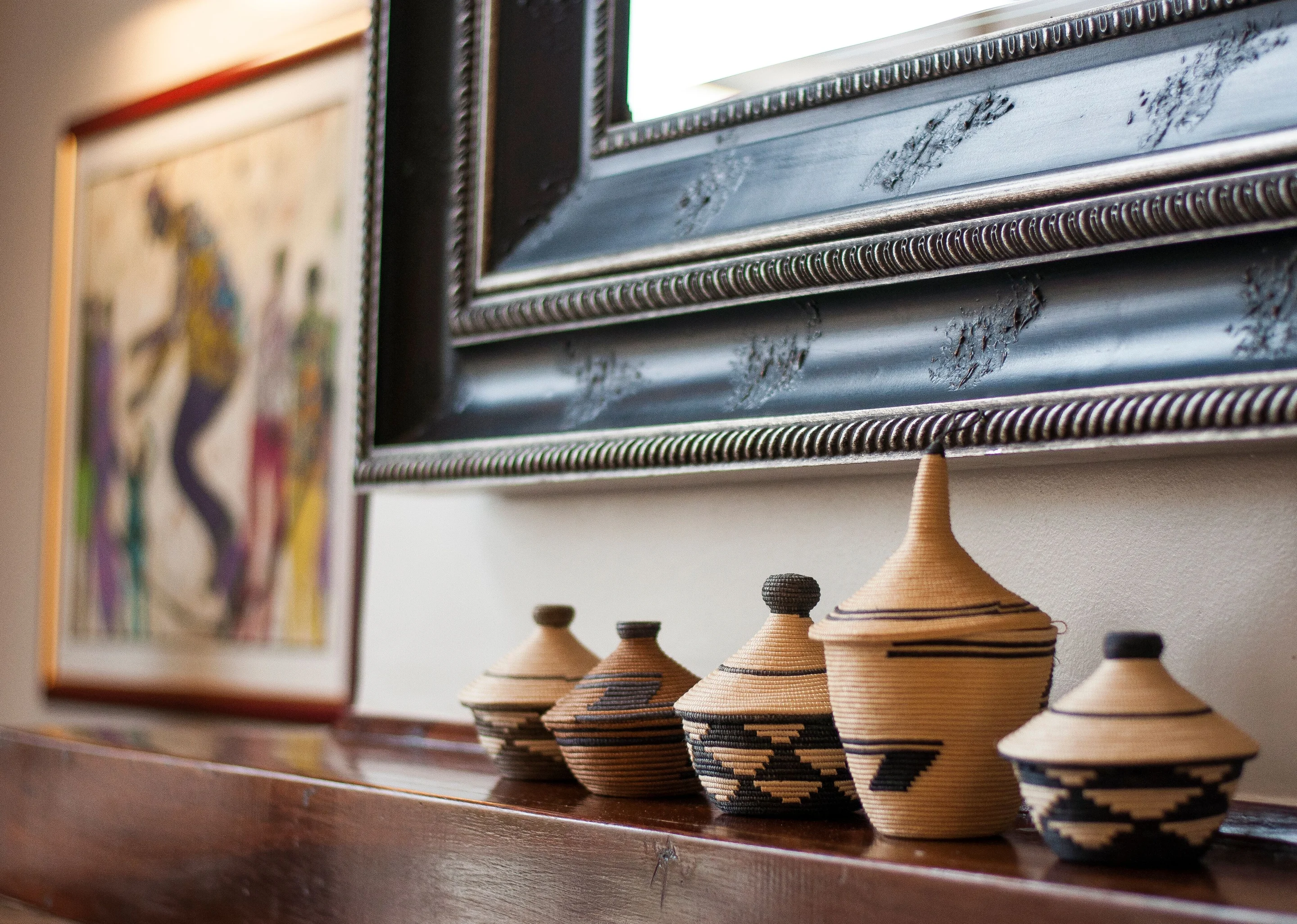 Woven lidded baskets arranged beneath carved dark-framed mirrors and a colourful artwork