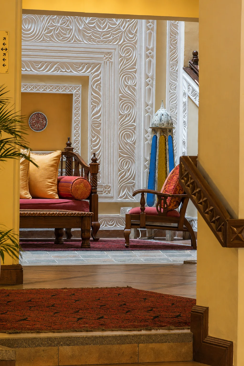 View through the Heron Hotel lobby toward carved plasterwork, timber seating and a coloured glass lantern