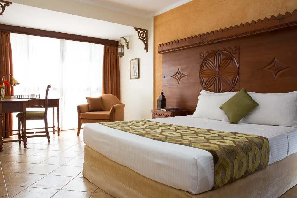 Bedroom with a carved timber headboard and patterned cushions — Heron Portico Hotel