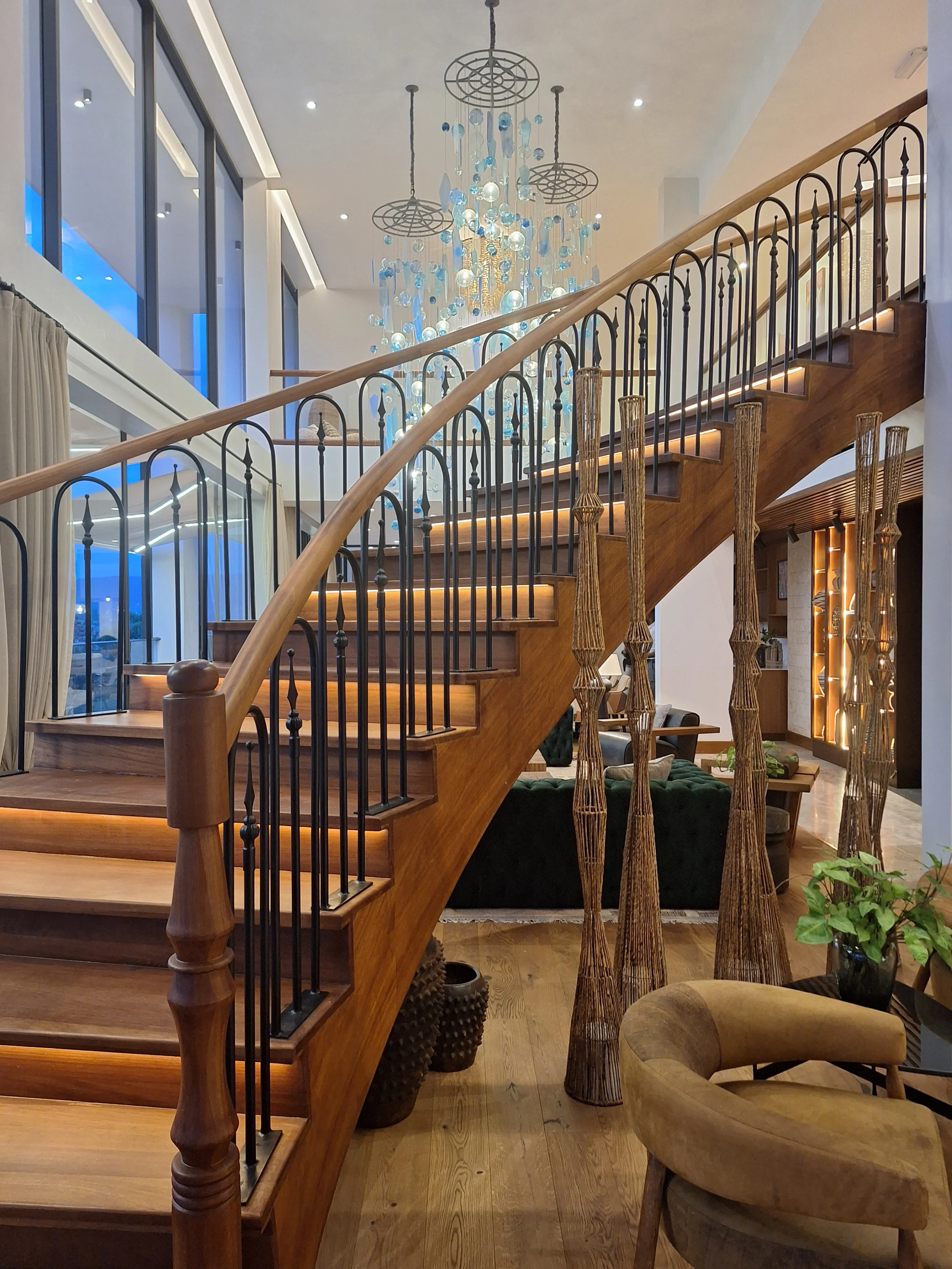 Curved timber staircase beneath the suspended blue glass chandelier at Sky Villa Soleil