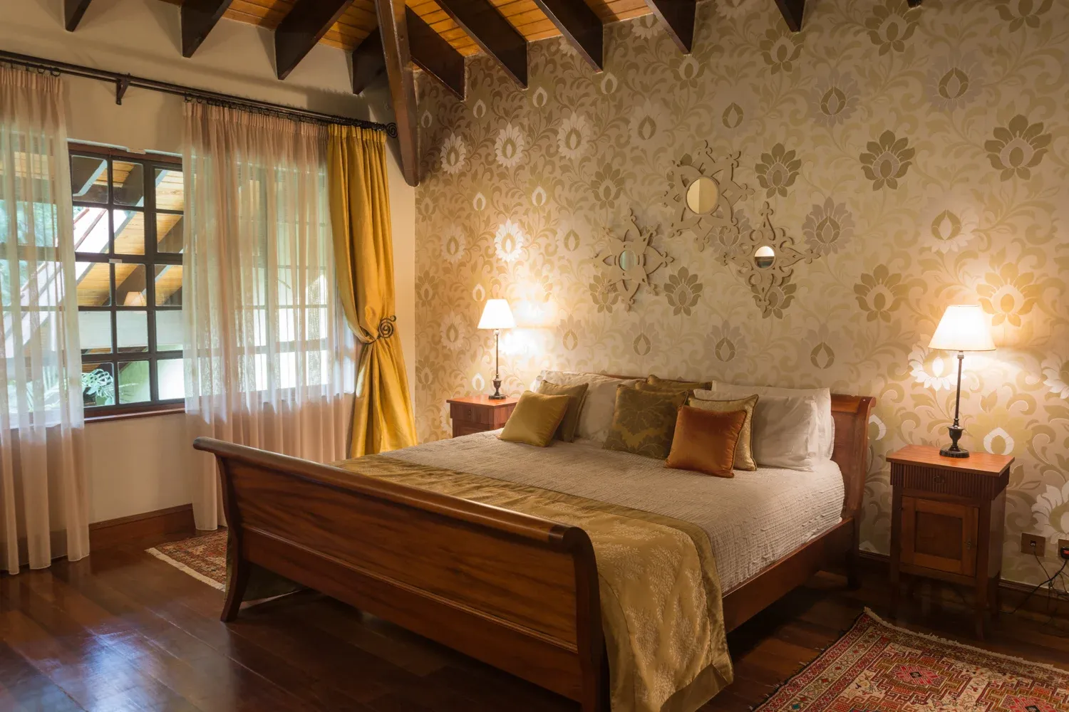 Bedroom with timber bed, patterned wall and yellow curtains in Mbogani