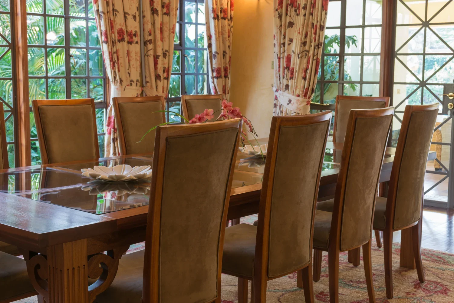 Dining table and high-backed chairs beside garden-facing windows in Mbogani