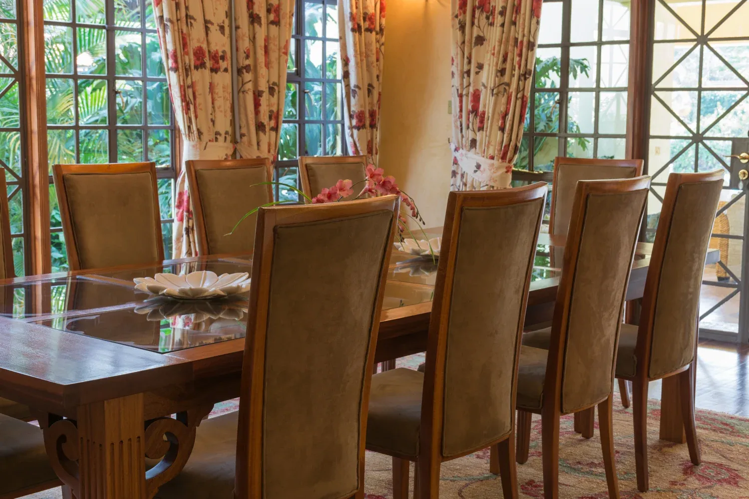 Dining table and high-backed chairs beside garden-facing windows in Mbogani